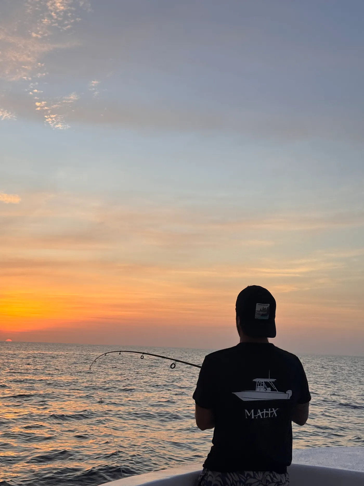 A guest in a Malix shirt watching the sunset over the Pacific from the boat